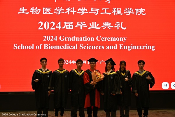 Graduates and faculty posing together on stage at a college graduation ceremony