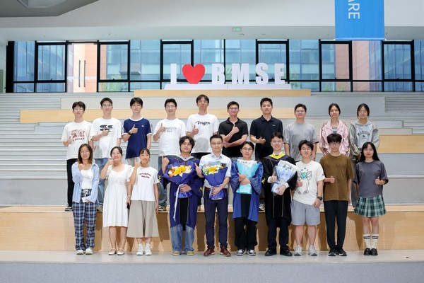 Lab members and graduates holding bouquets in front of the BMSE sign.