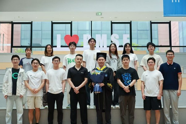 A graduate in cap and gown holding a bouquet with lab members in front of the BMSE sign.