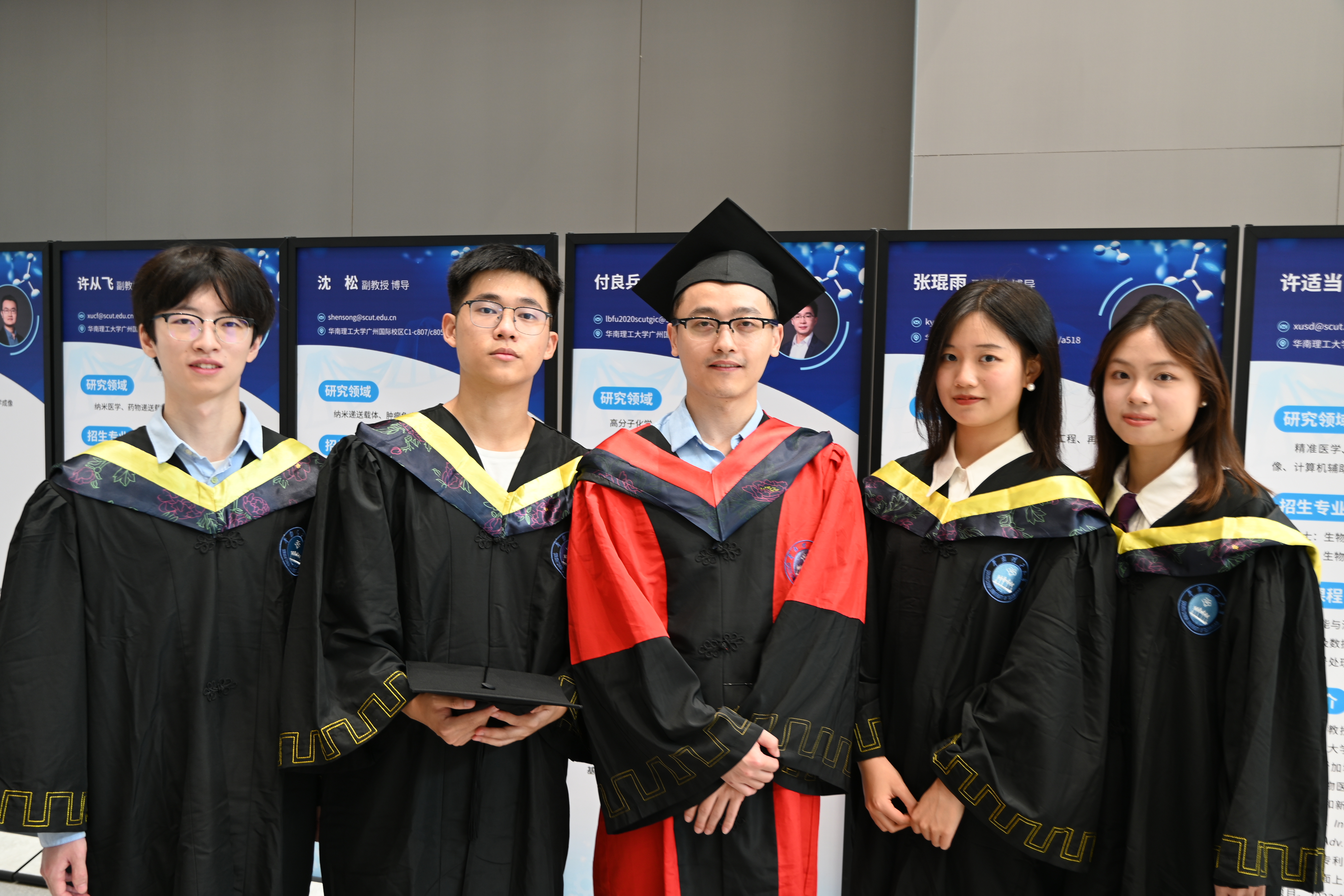 Five people in academic gowns posing together in front of a display.