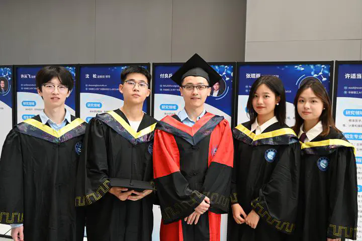 Five people in academic gowns posing together in front of a display.