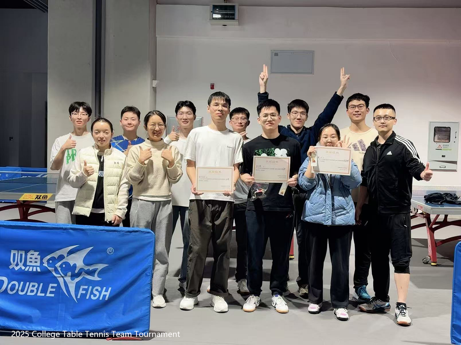 Tournament participants posing with certificates beside indoor table tennis tables.
