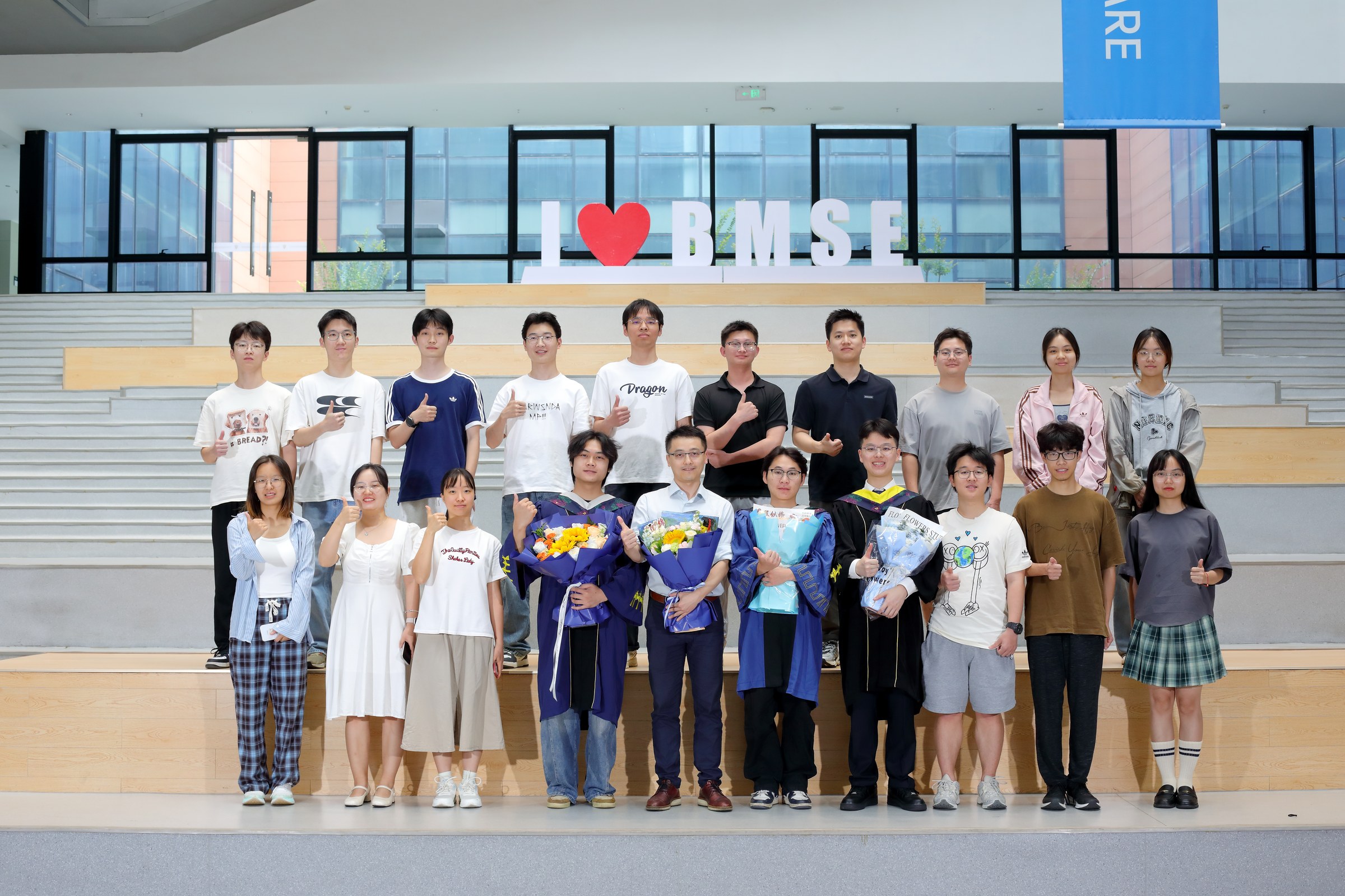 Lab members and graduates holding bouquets in front of the BMSE sign.