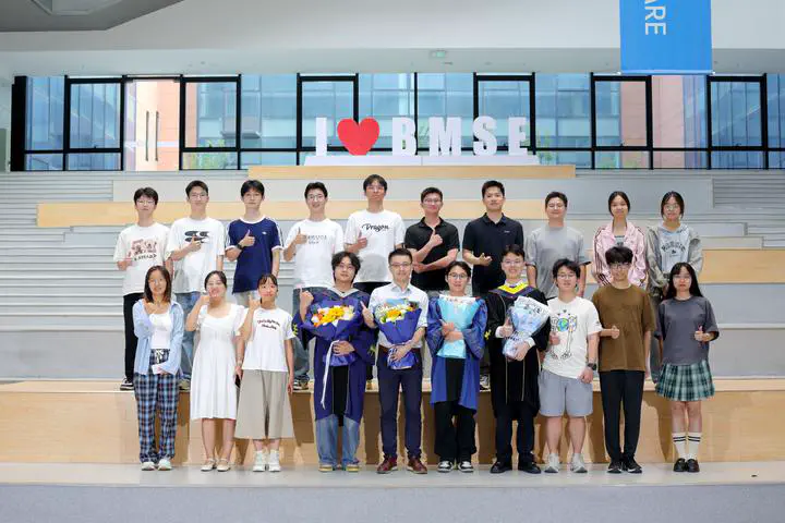 Lab members and graduates holding bouquets in front of the BMSE sign.